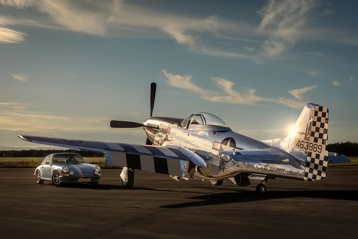 Porsche 911 Rat und P-51 Mustang Flugzeug bei einem Autofotoshooting auf einem Flugfeld.